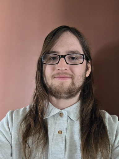 A male with brown hair and hazel eyes wearing a white collared shirt.